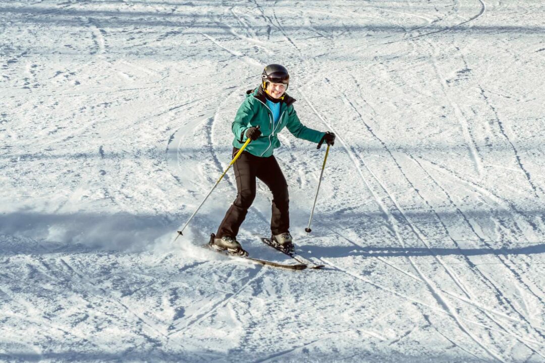 Woman skiing downhill on a snow-covered slope in Sweden, with skis and poles.