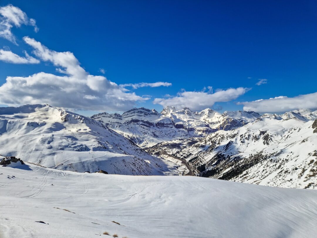 Snowshoeing and winter hiking route across a snow-covered mountain with distant peaks under a blue sky
