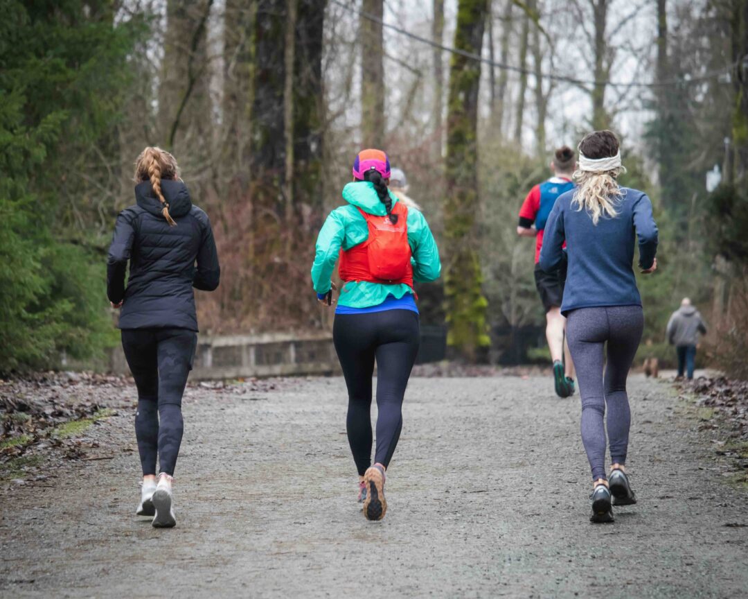 Women jogging on a gravel path through a wooded forest in outdoor winter conditions
