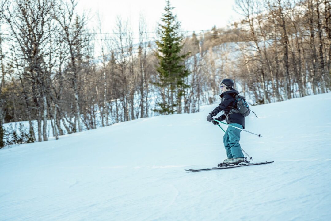Woman downhill skiing on a snowy slope through a forested winter landscape