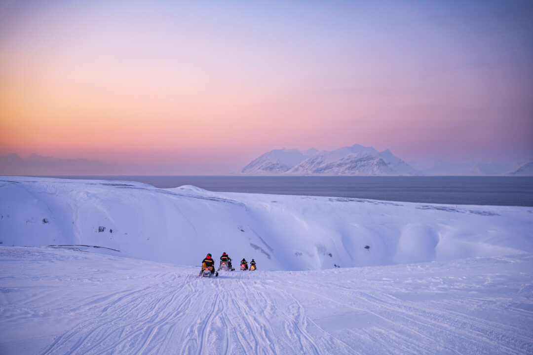 Women sledding across snow in Svalbard at dusk with mountains in the distance