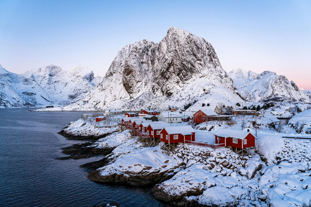 Snowy Lofoten fjord village with red cabins and dramatic mountains under a clear winter sky