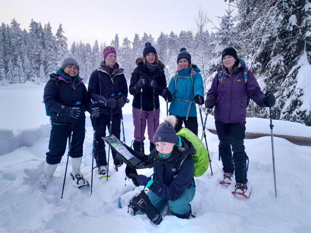 Group of winter snowshoeing hikers in Finland, posing in snowy forest with wooden trail clearing behind them