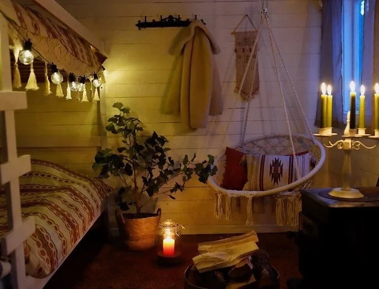Cozy winter camping cabin interior with lit candles, bed and hammock chair