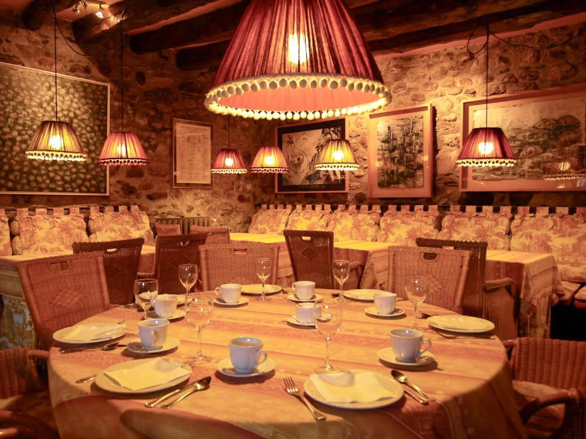 Cozy Pyrenees restaurant dining room with set tables and warm pendant lamps in stone interior