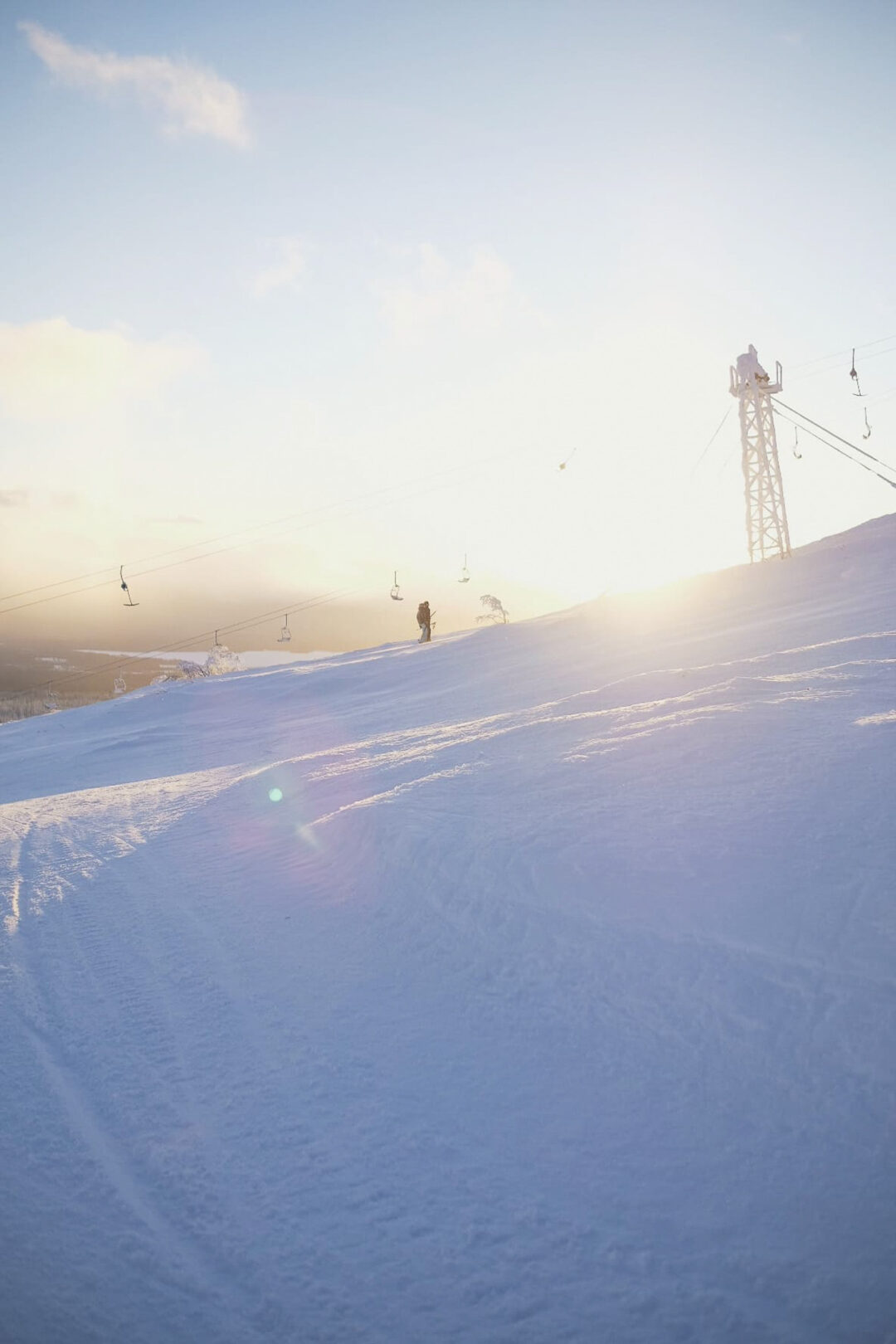 Skier on a downhill slope beside chairlift poles at a ski resort at sunset