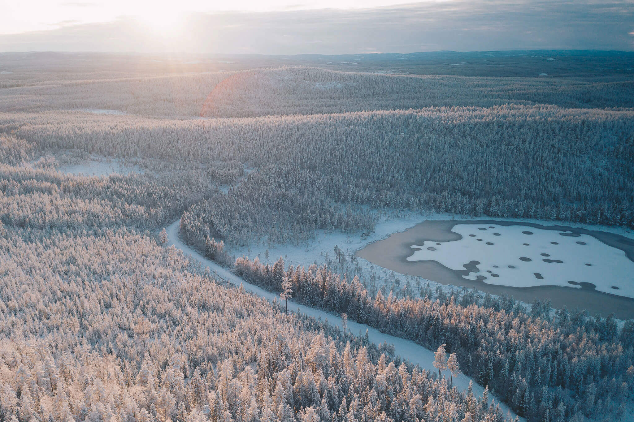 Aerial view of snowy pine forest and frozen lake in Lapland during winter