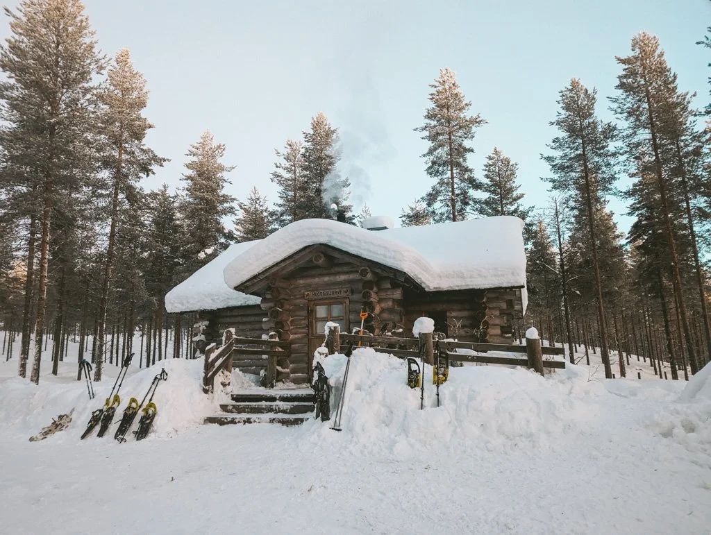Snowshoe trail in Finland beside a snowy log cabin in a pine forest during winter dusk