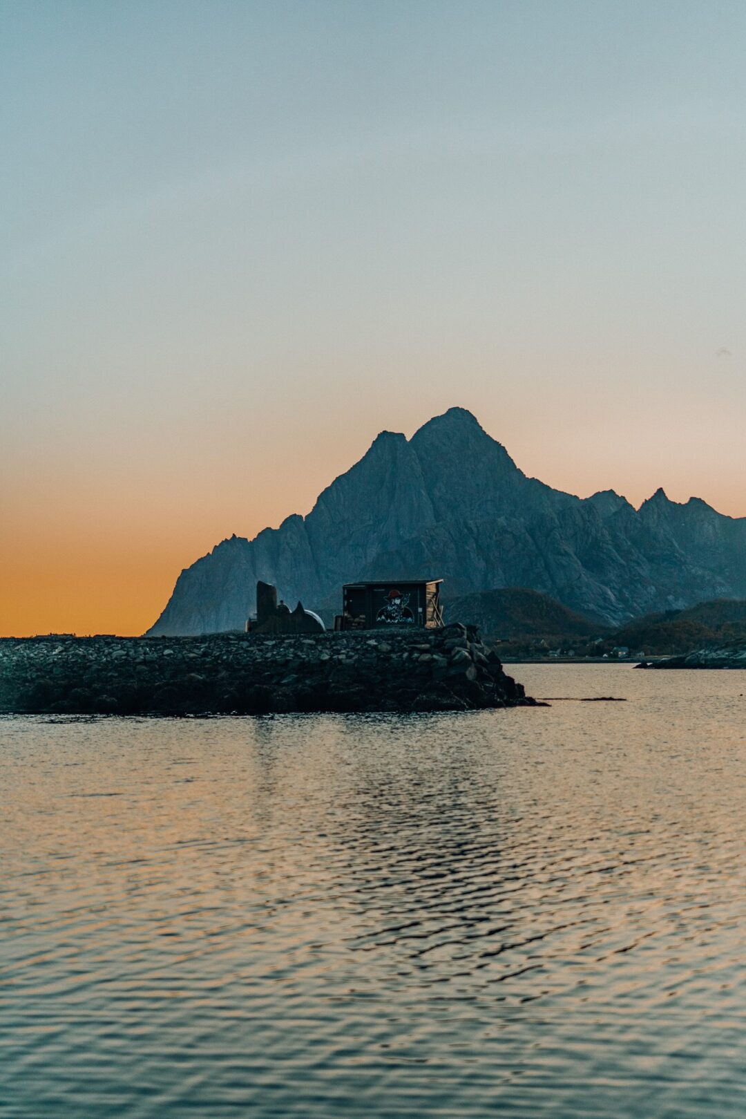 Sunset over a calm fjord with rugged mountains and a rocky islet on the water