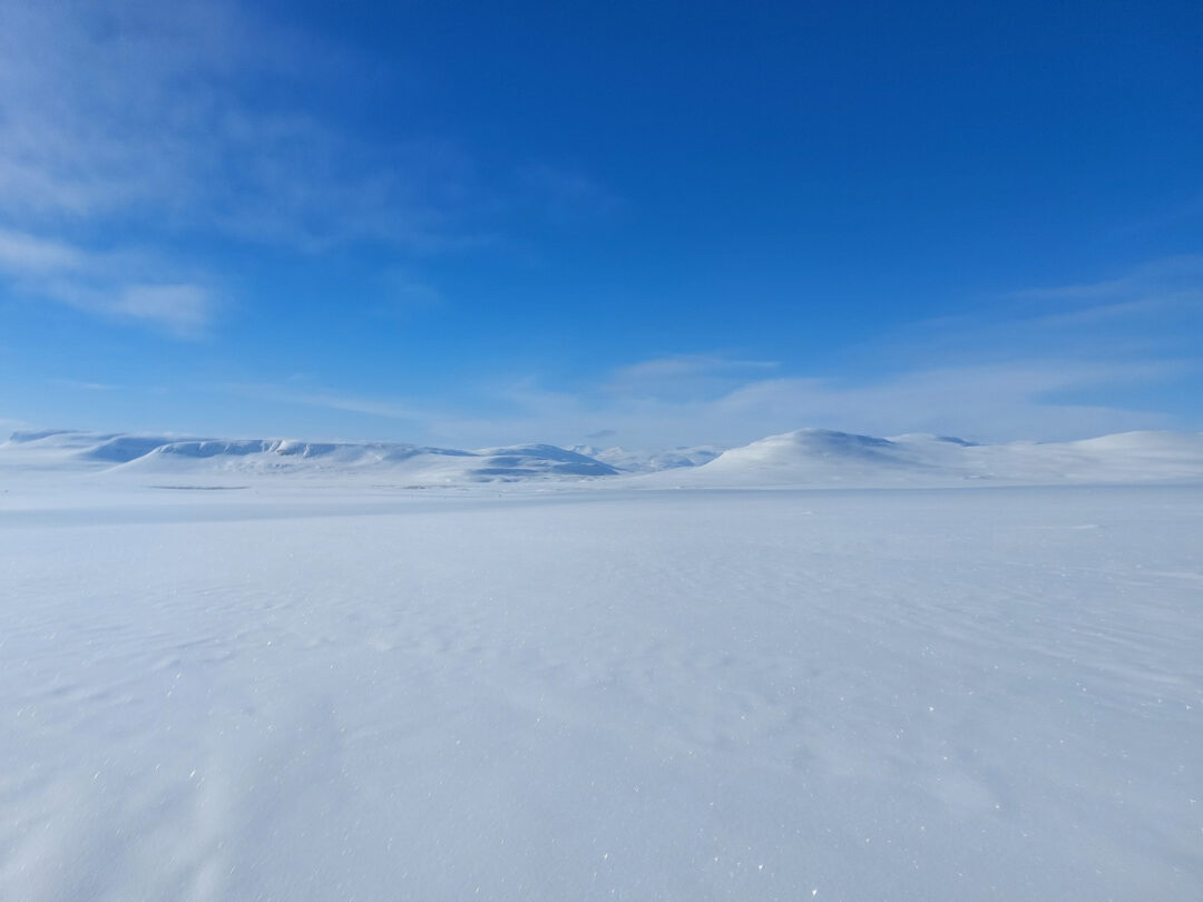 Snow-covered Arctic tundra with distant glaciers under a clear blue sky for hut-to-hut ski expeditions.