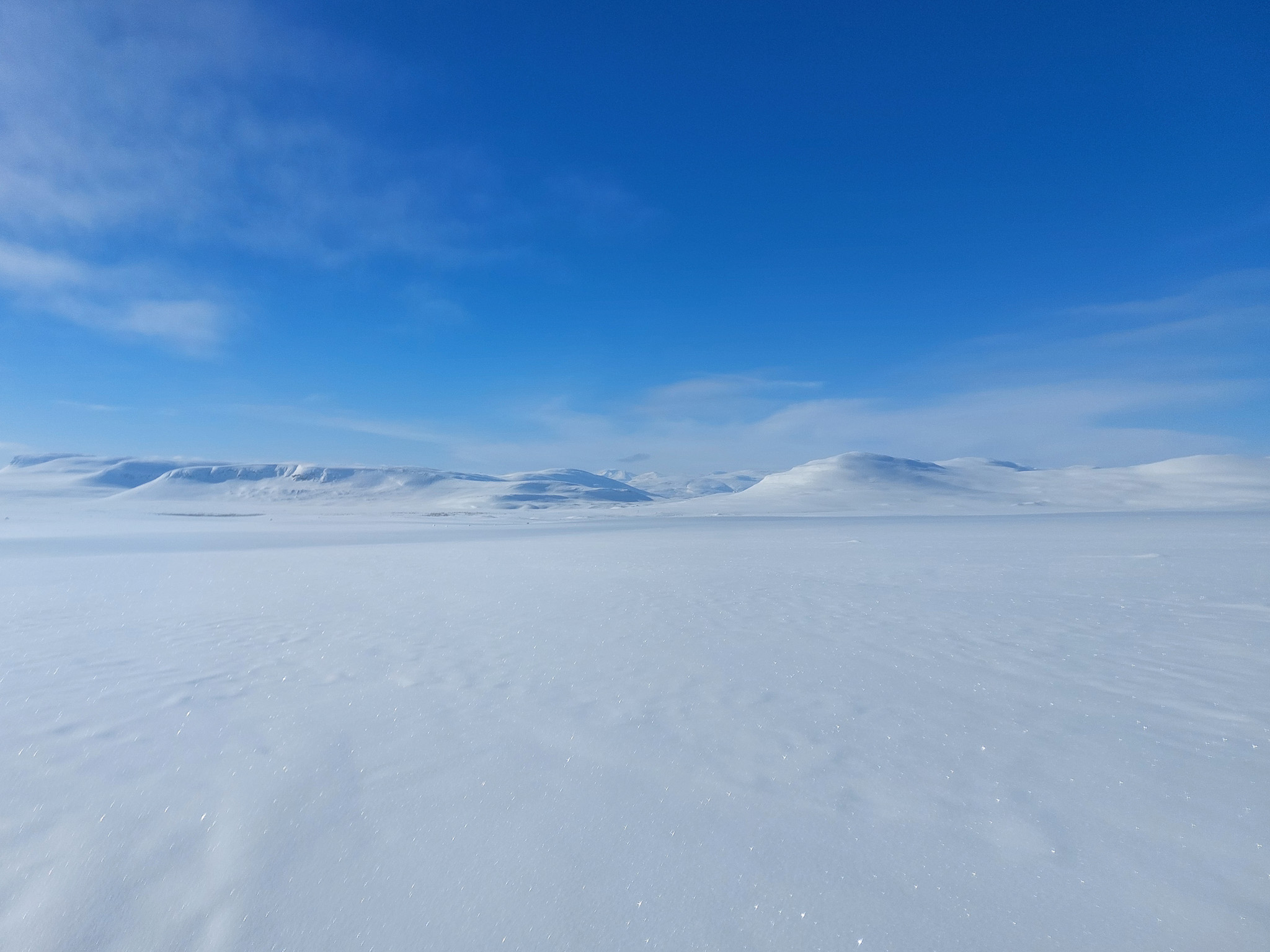 Snow-covered Arctic tundra with distant glaciers under a clear blue sky for hut-to-hut ski expeditions.