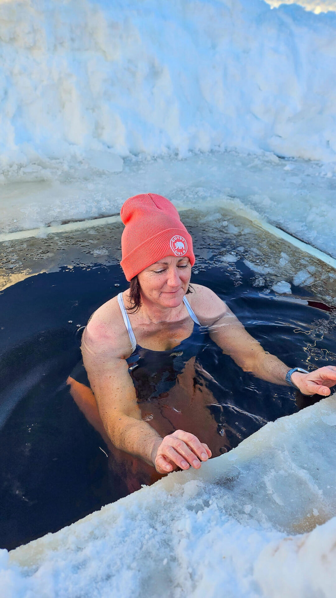Woman in a red beanie takes a cold plunge in an outdoor winter spa pool, Norway, after cross country skiing