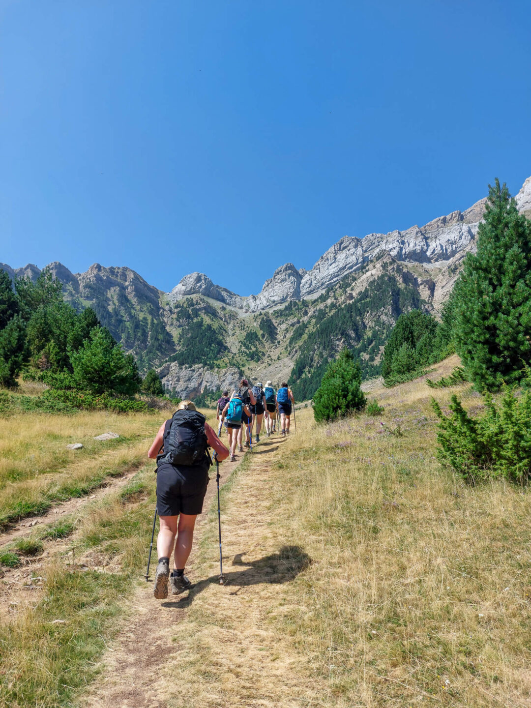 Women hiking along a mountain trail in the Pyrenees under clear blue sky