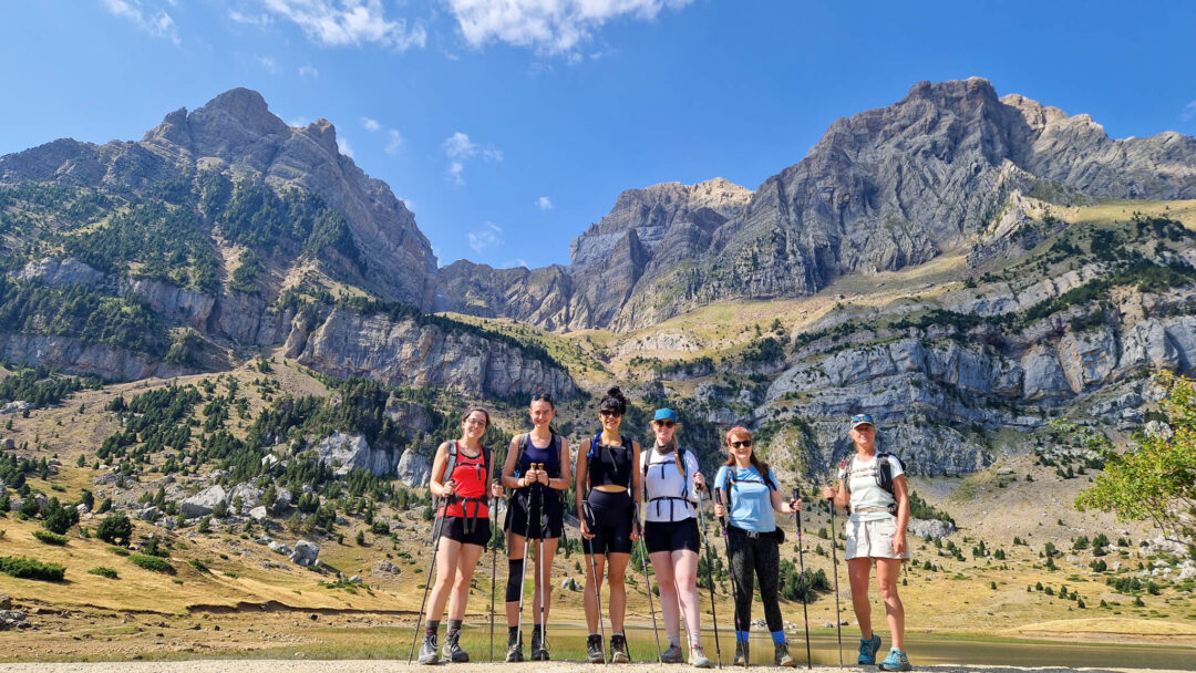 Women hiking in the Pyrenees mountains with a guide, standing on a trail under a blue sky