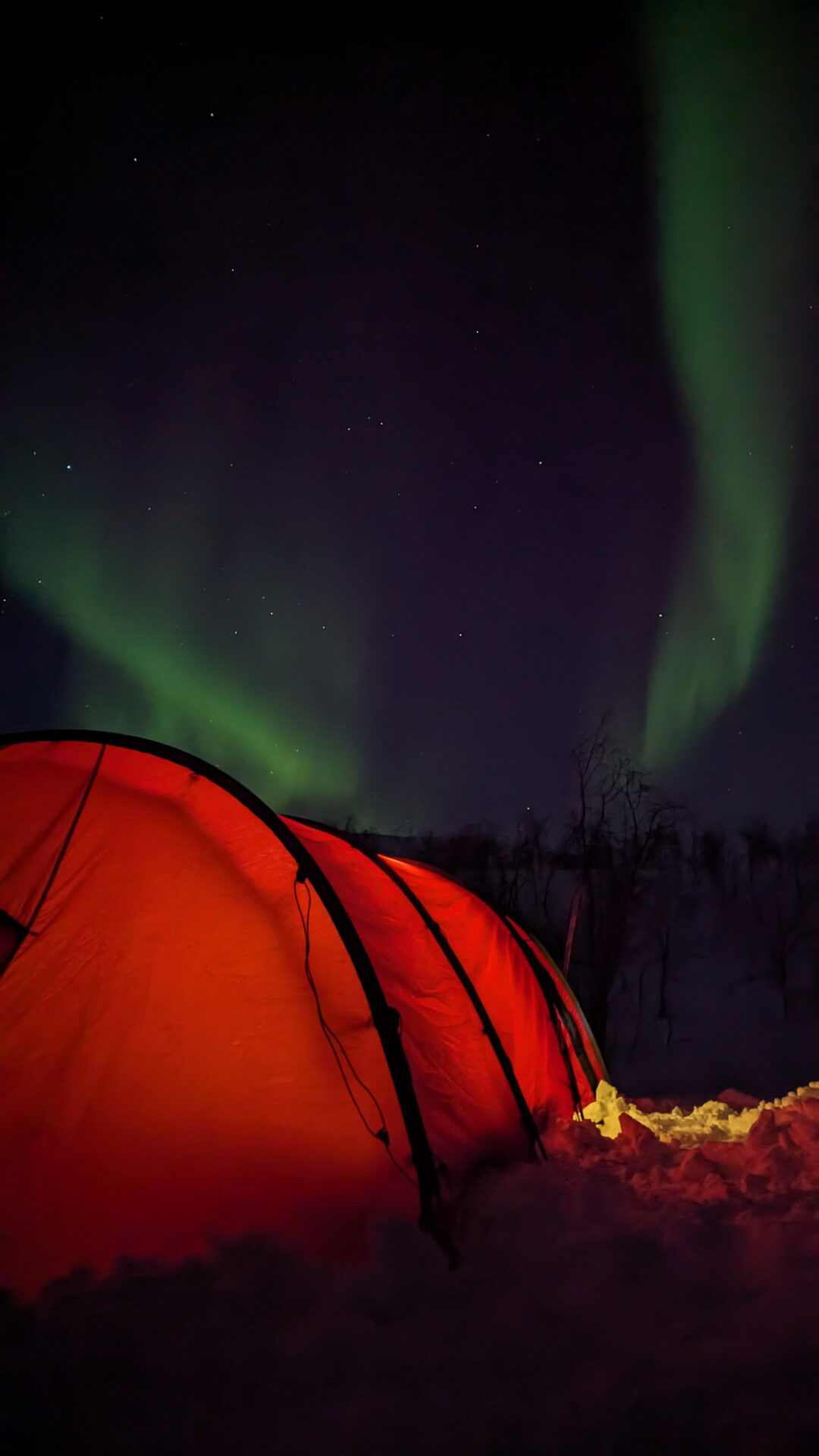 Aurora borealis over a red ski expedition tent on snowy Arctic ground at night