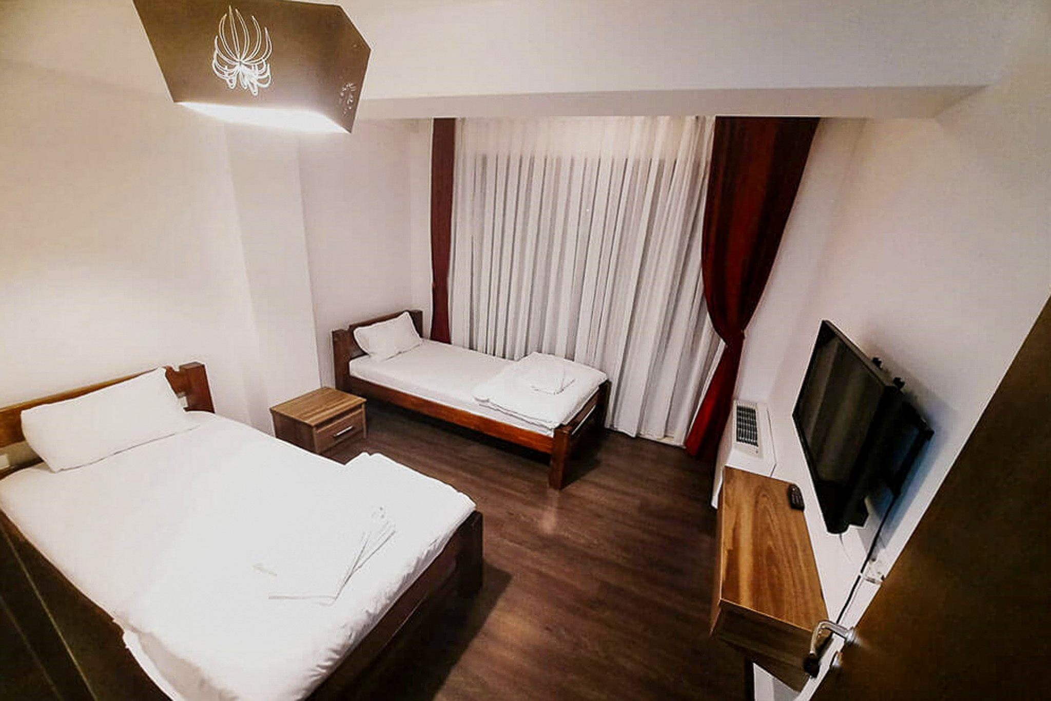 Twin hotel room with two beds, curtains, and a wall-mounted TV