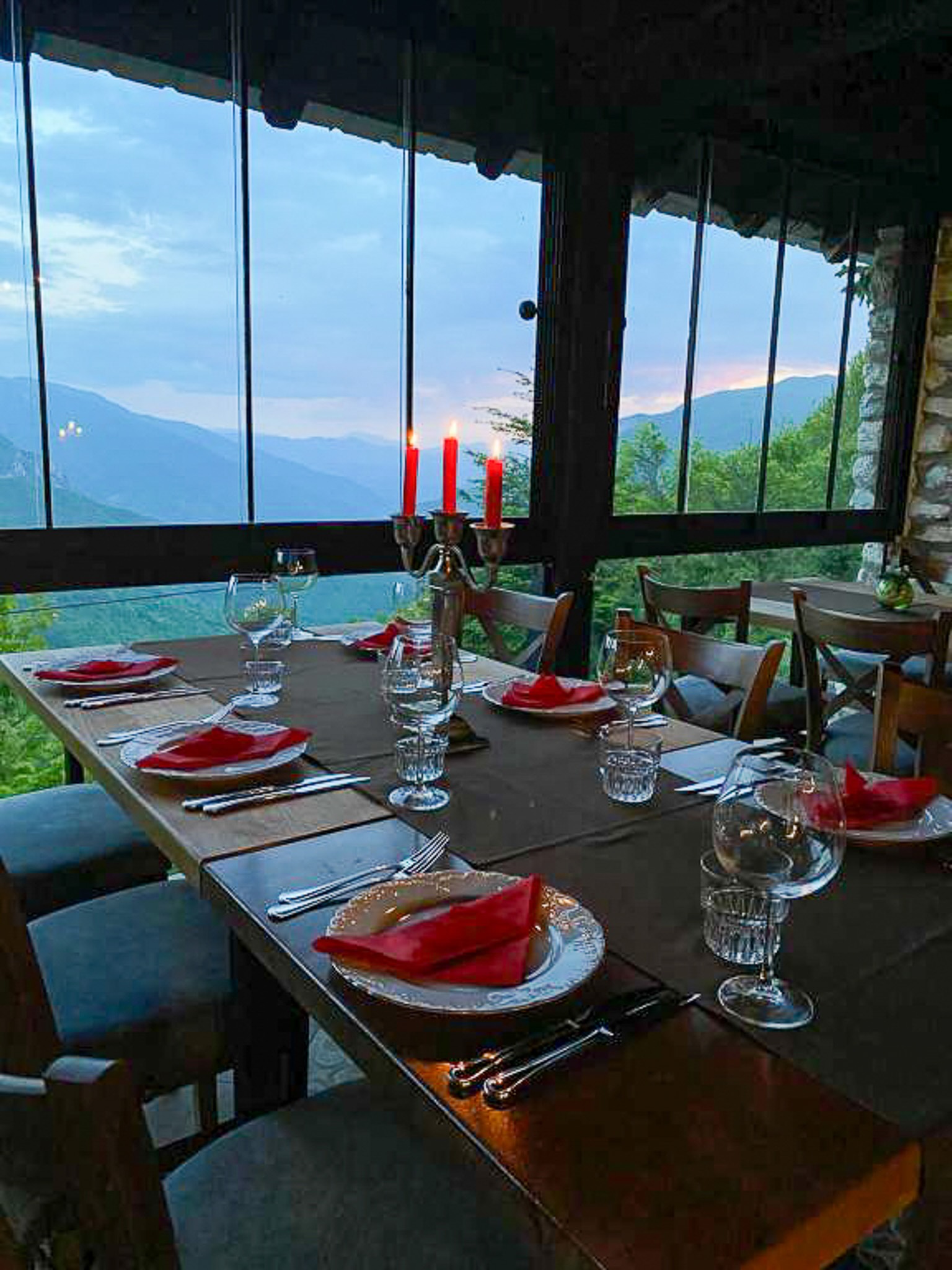 Candlelit dining table set inside a lodge with a panoramic mountain view through large windows