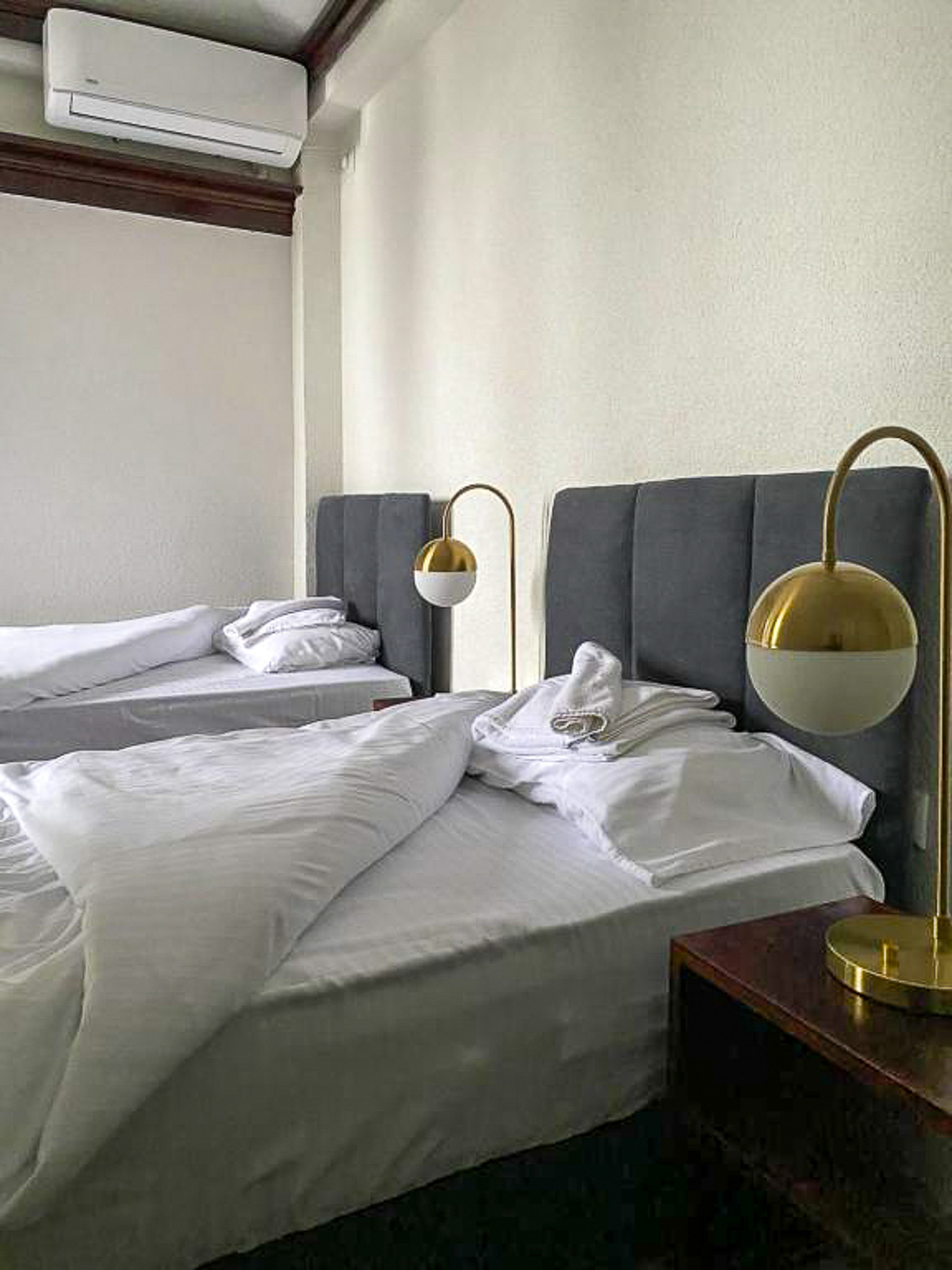 Unmade beds with grey headboards and gold bedside lamps in a hotel room