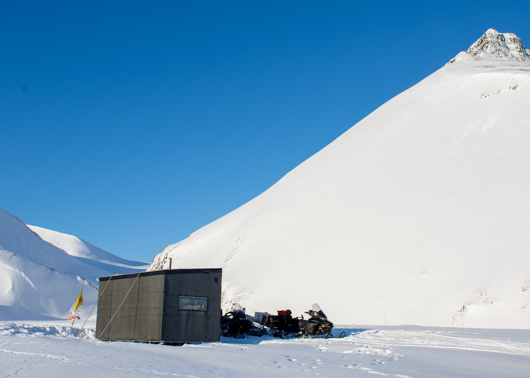 Snowmobiles parked beside an expedition shelter on Svalbard’s snowy plain under a clear blue sky