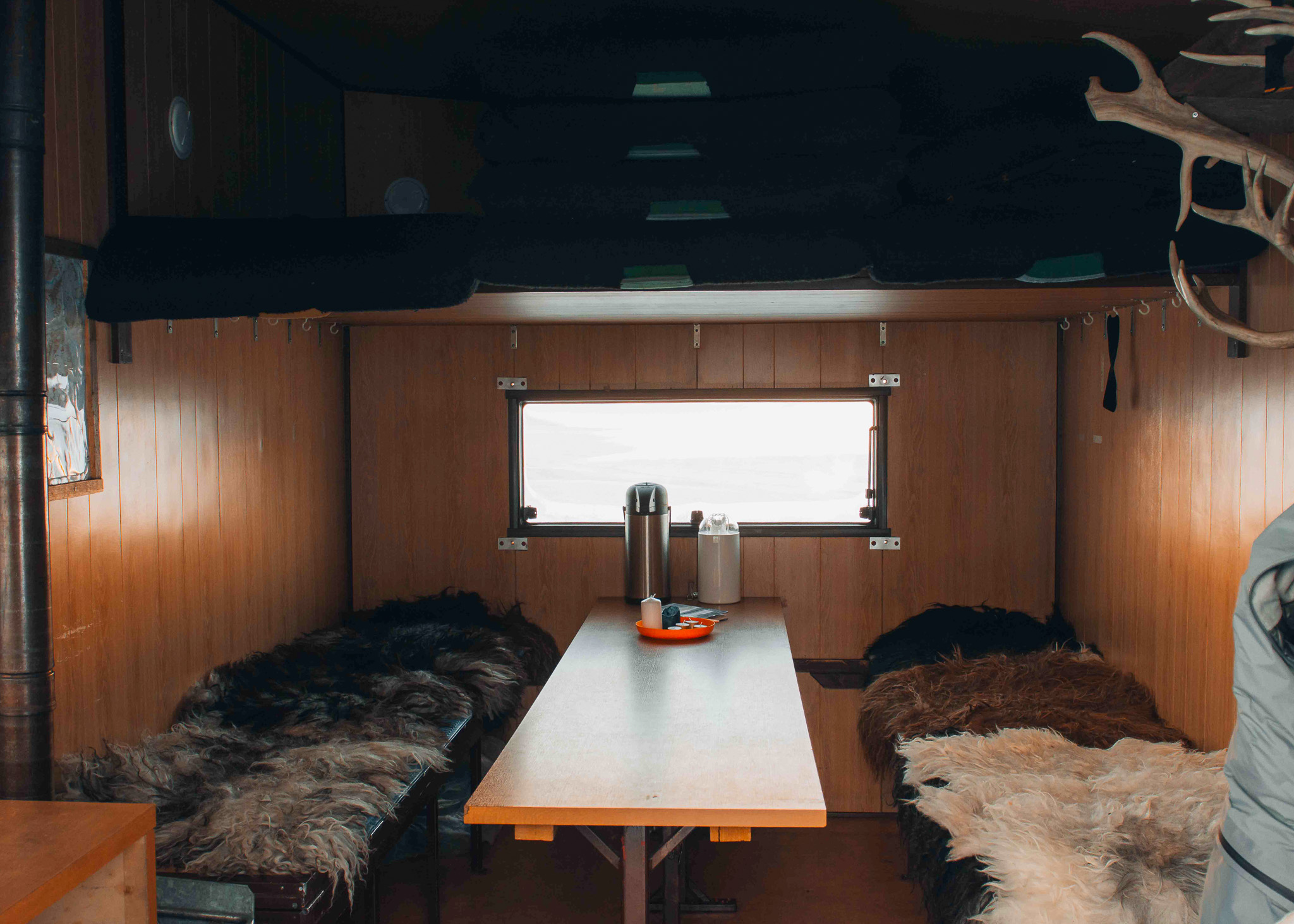 Snowmobile camper cabin interior with table, warm fur bedding and thermos by a window