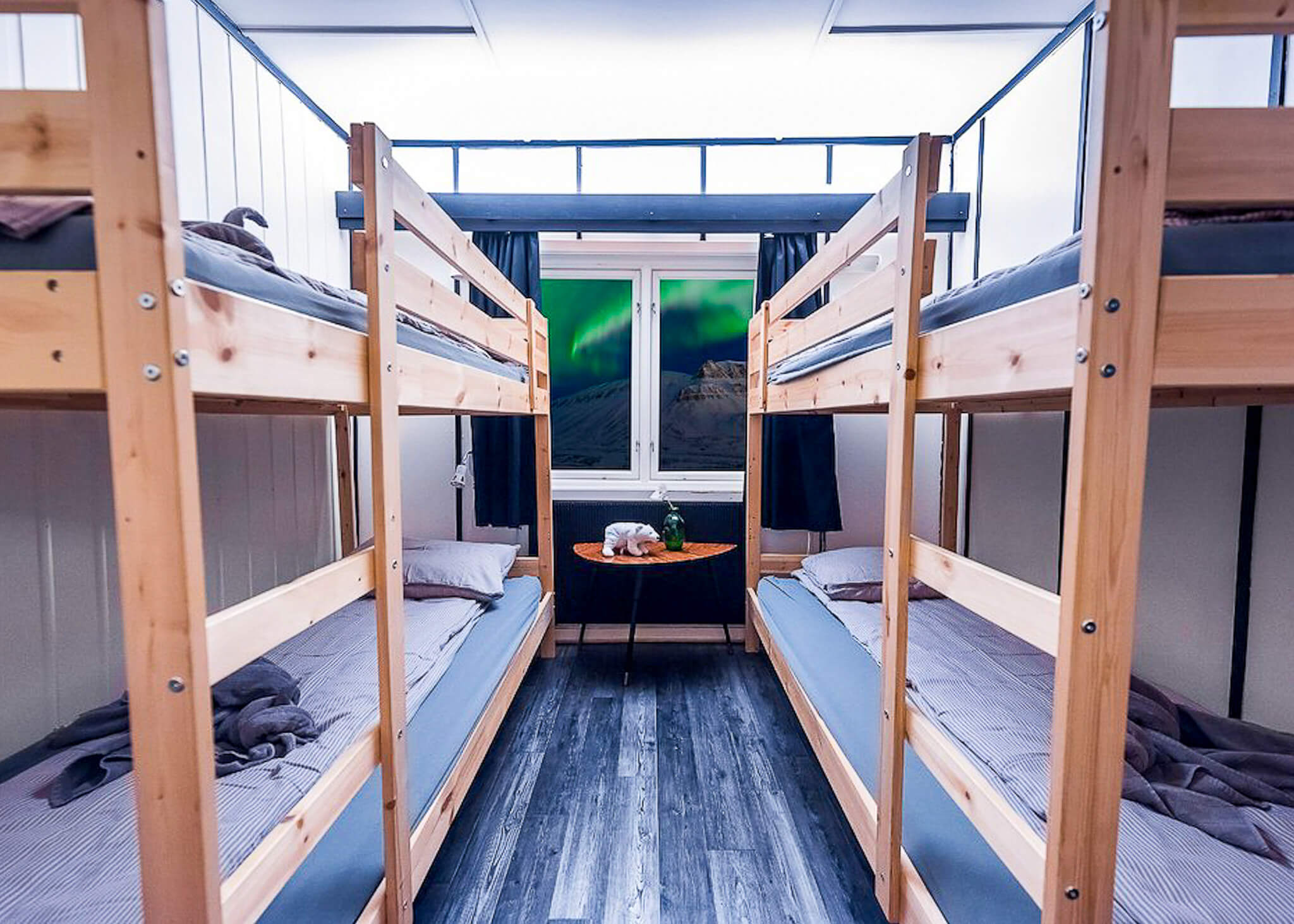 Wooden cabin bunk beds with snowy mountain view through the window, ideal for a Svalbard expedition stay