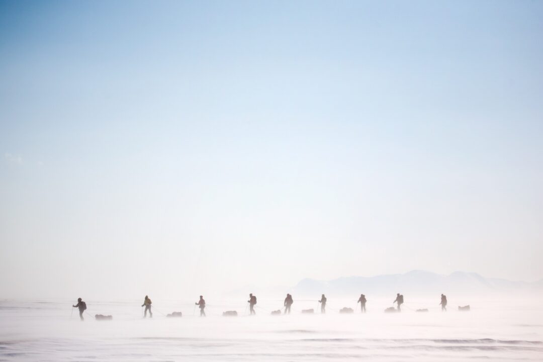 Women walking across a snowy Arctic landscape on Svalbard, in mist and low light.