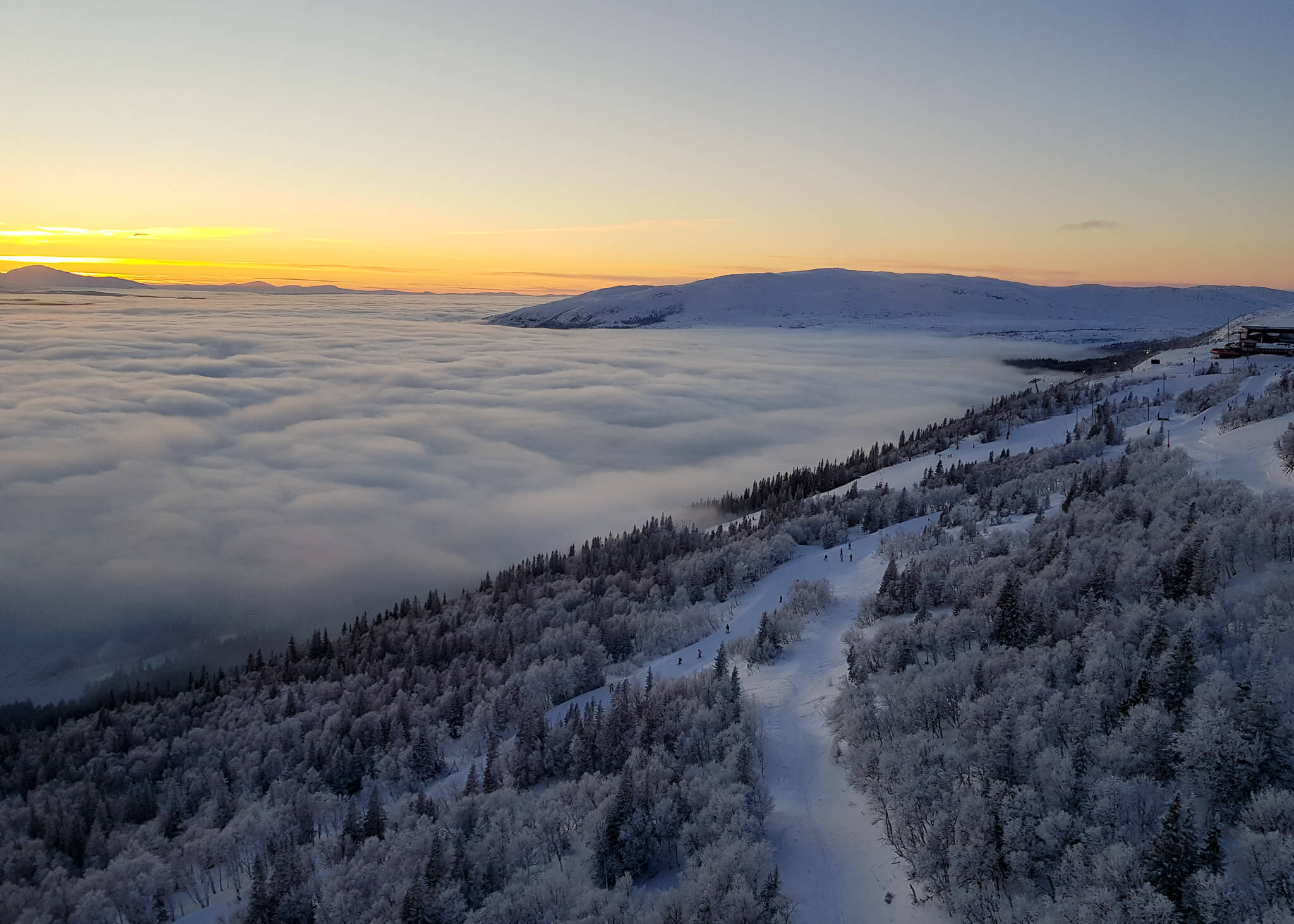 Snowy Swedish mountains at sunrise, ski touring tracks over a forested valley above the clouds