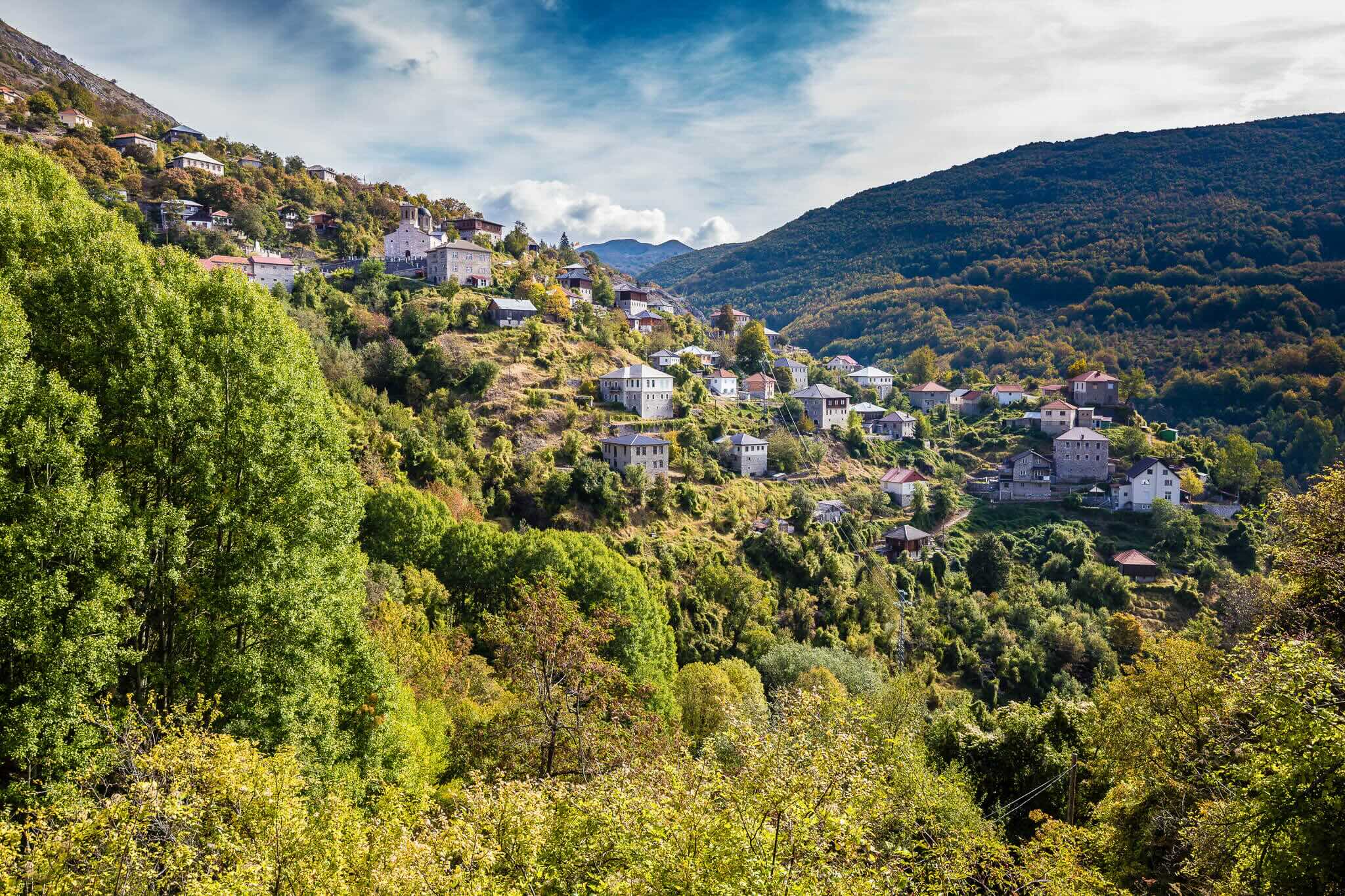 Scenic hillside village in a mountain valley with lush green forests, suitable for guided hiking in North Macedonia