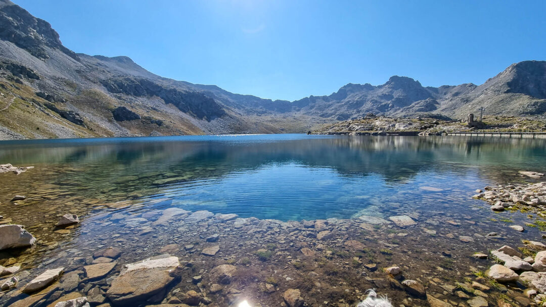 Mountain lake with clear water and rocky shore, surrounded by Pyrenees-style valley peaks and hills