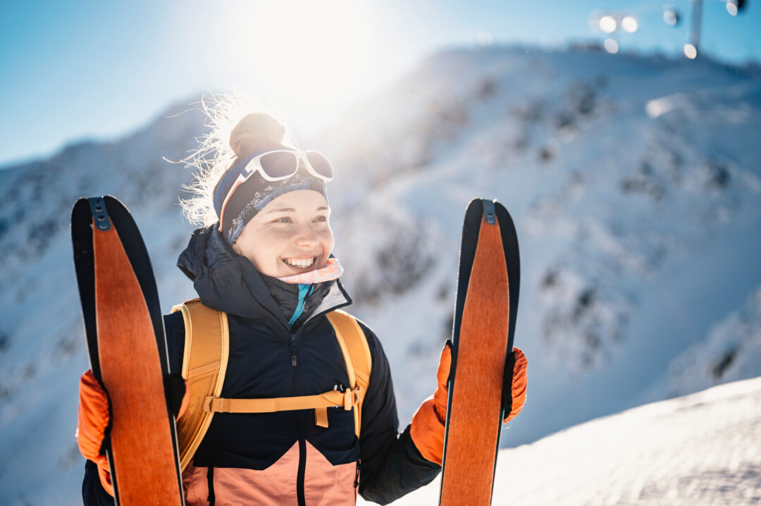Smiling ski tourer in winter sun with skis on snowy slopes of Sweden’s mountains