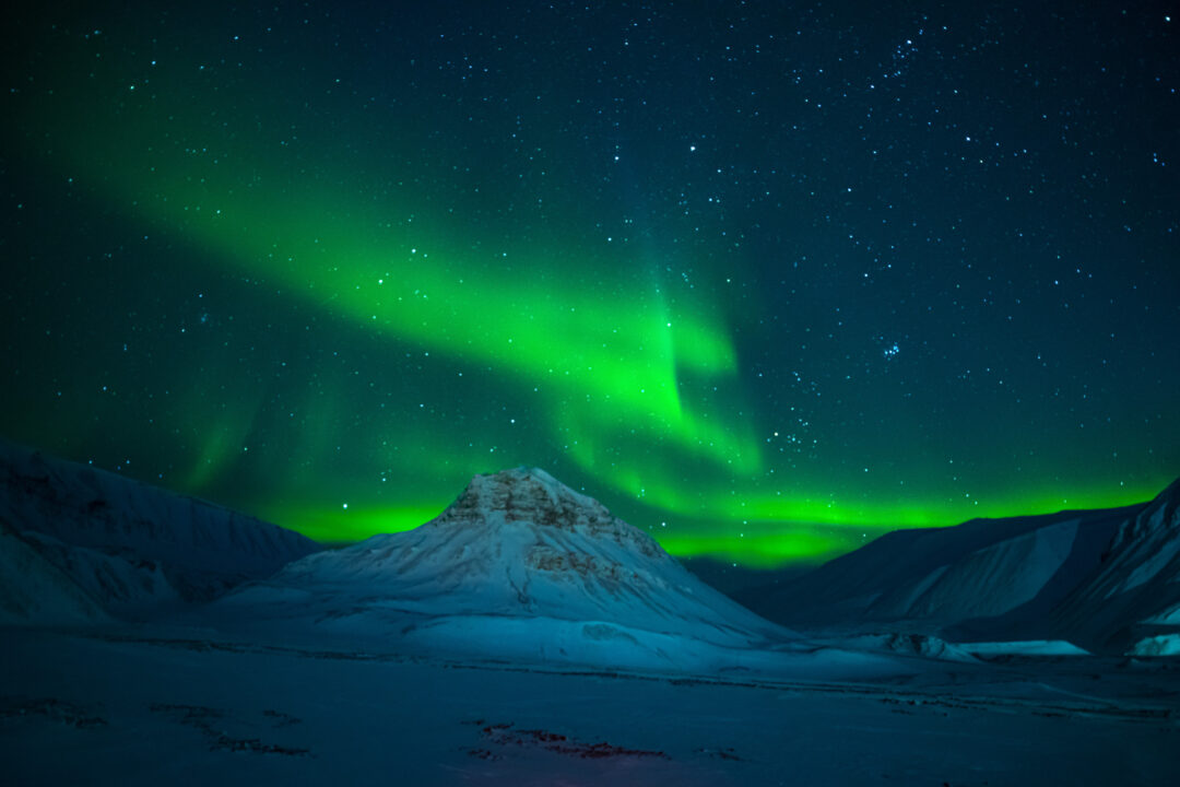Northern lights over snowy mountains in Svalbard, Arctic winter night sky