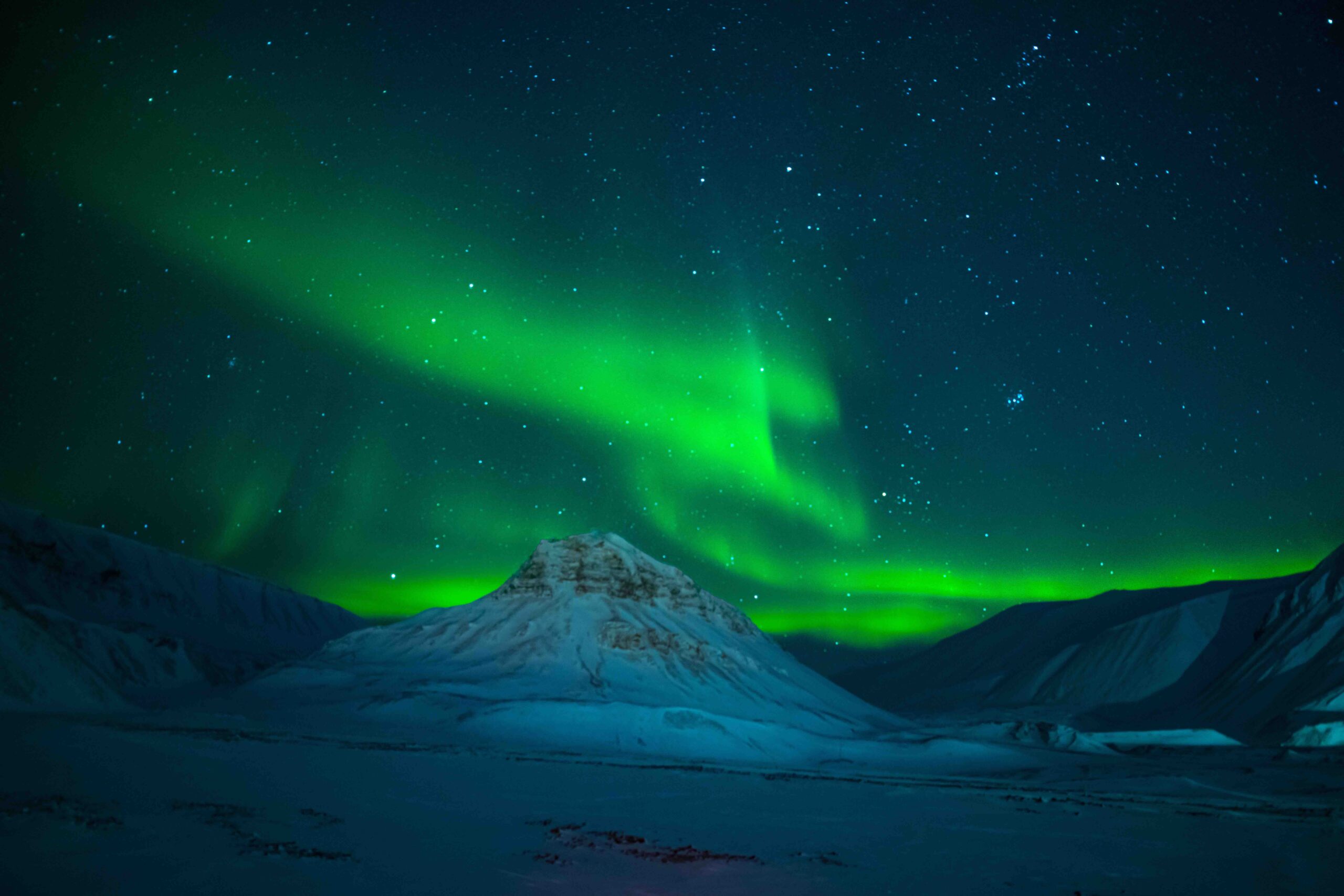 Green aurora borealis over snow-covered Svalbard mountains under a starry night sky