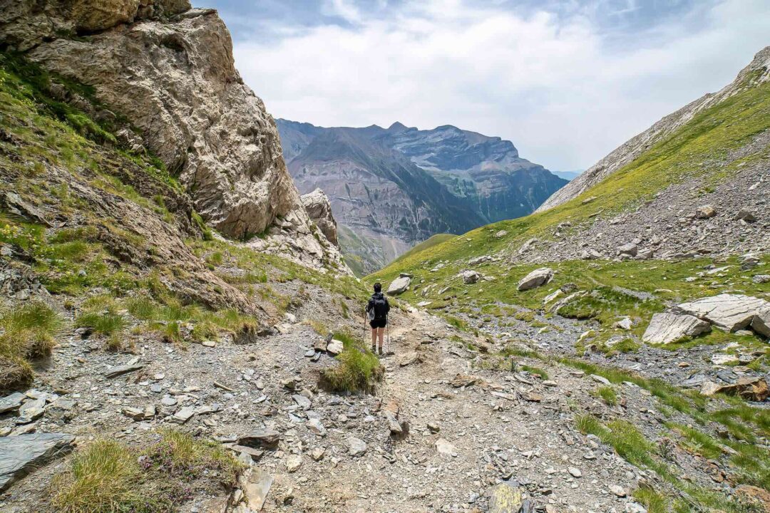 Woman hiking a rocky trail in the Spanish Pyrenees mountain valley, with peaks and green slopes in view
