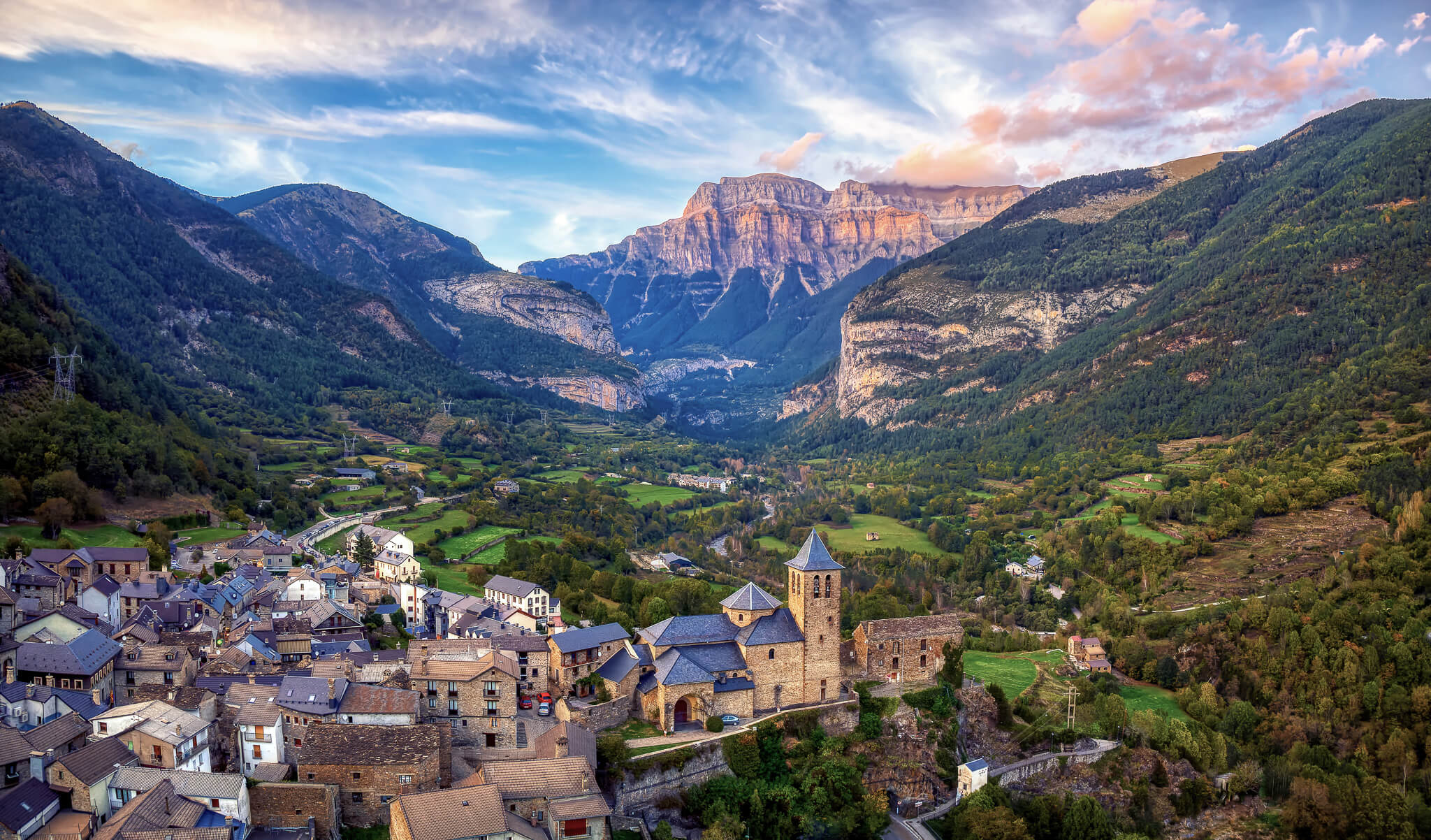 Sunset view of a Pyrenees mountain valley with a village and fortress in the distance