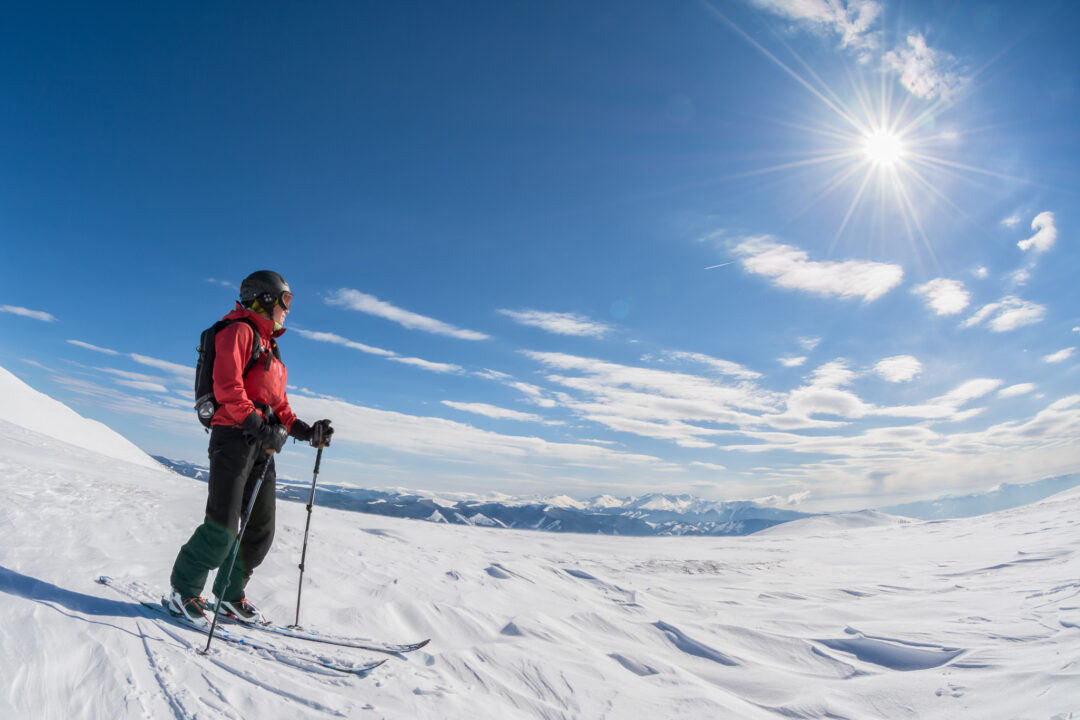 Ski tourer hiking across snowy slopes in bright sunshine with skis and poles in Sweden