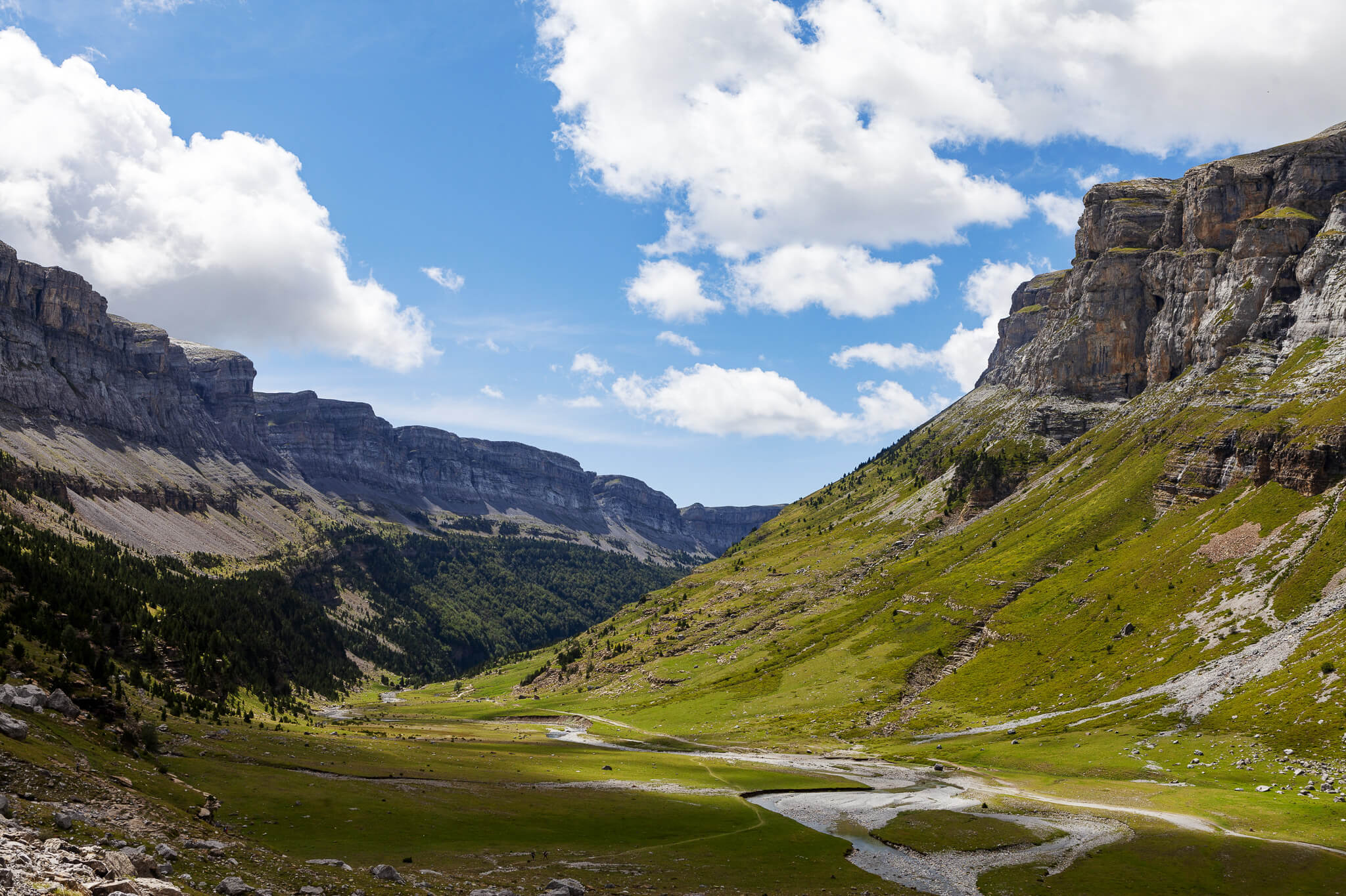 Mountain hiking landscape with winding valley road between rocky peaks and green slopes under a blue sky