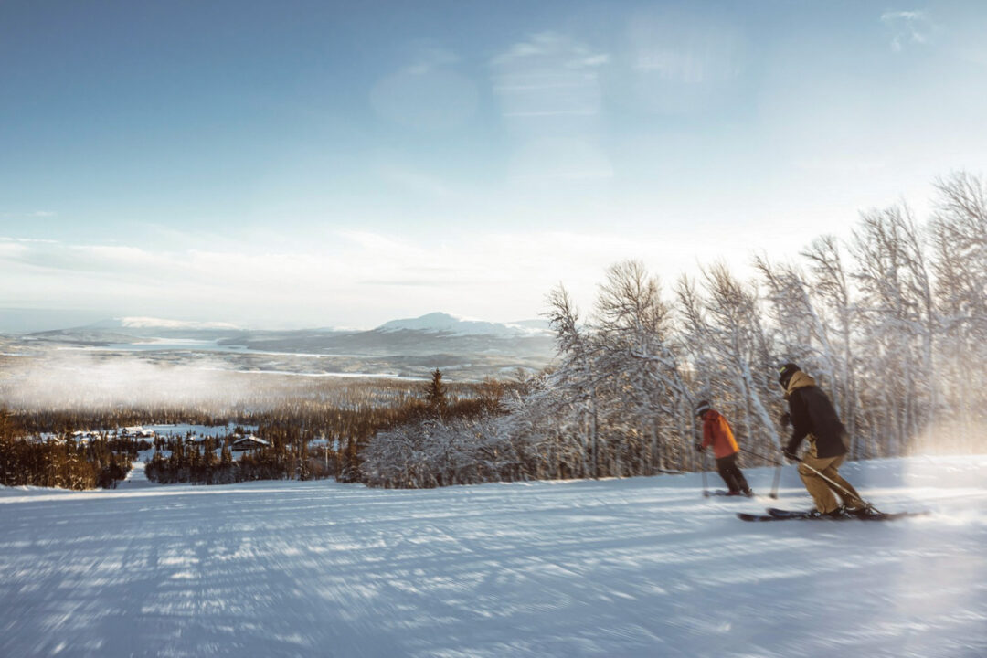 Downhill skiers carving through fresh snow on a Swedish slope with a scenic winter valley view