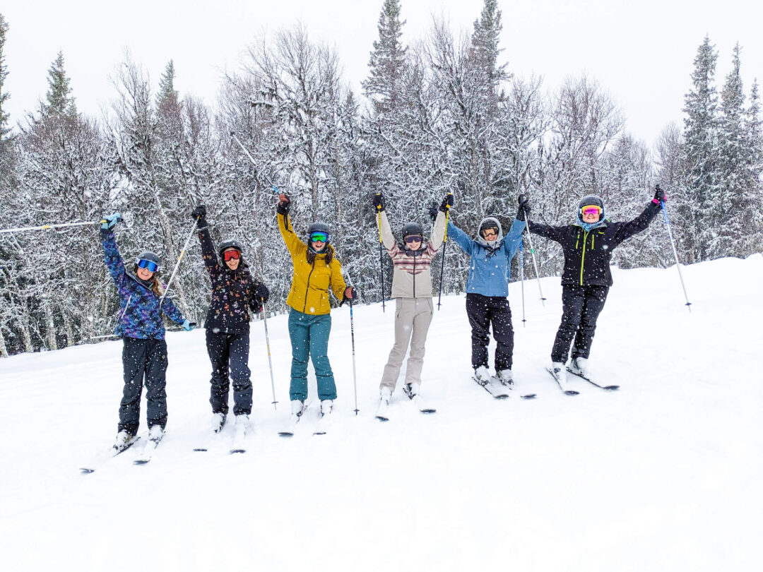 Group of beginner skiers on a snowy downhill slope in Sweden, arms up in celebration