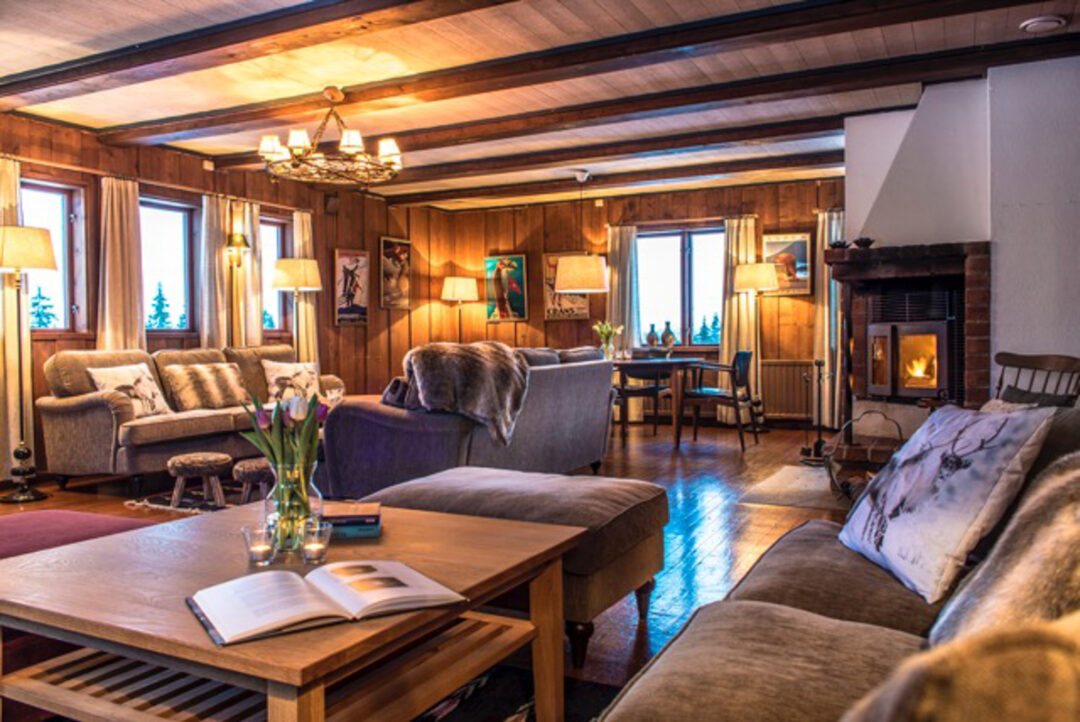 Cozy Swedish ski lodge living room with fireplace, wooden furniture and warm evening light.