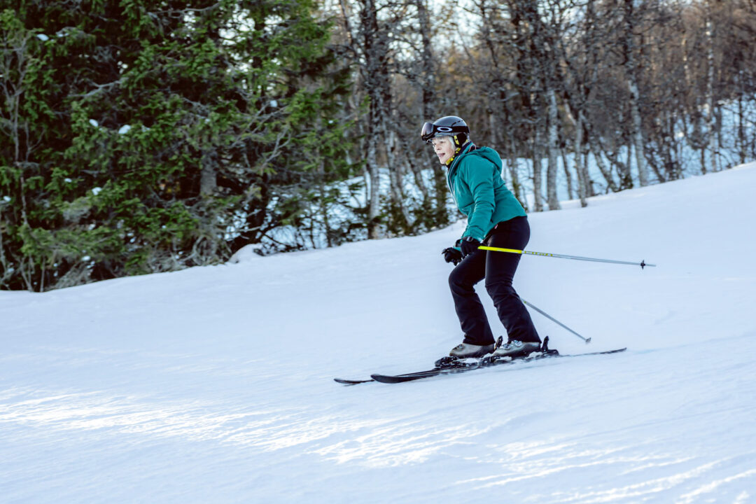 Skier carving beginner-friendly downhill ski slopes in Sweden’s snowy forest at first tracks.