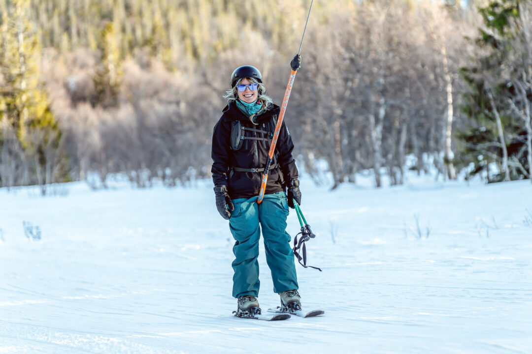 Beginner skier gliding downhill on a snowy piste in Sweden, holding ski poles through a pine forest