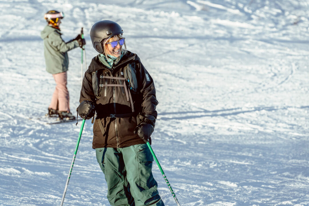 Beginner skier on a sunny Sweden downhill slope, wearing helmet and skis with another student in the background