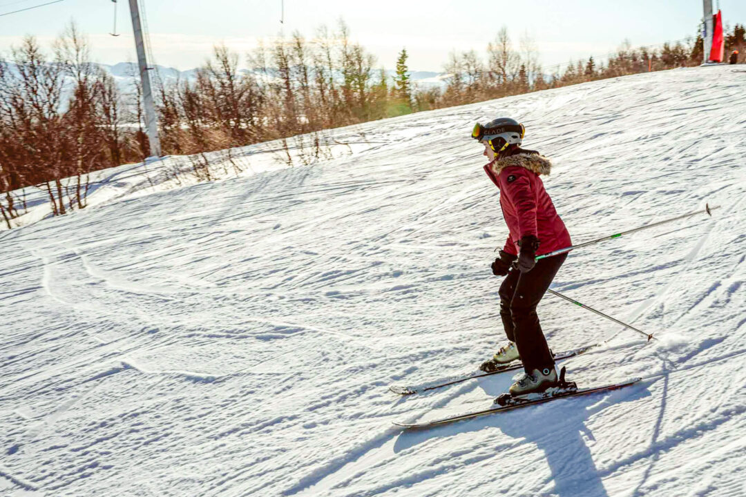 Beginner skier carving a groomed downhill slope in Sweden, wearing a helmet and skis in the winter snow