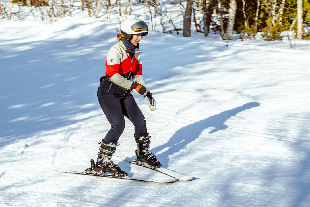 Beginner skier carving downhill on groomed snow in Sweden, wearing helmet and goggles on a ski resort trail
