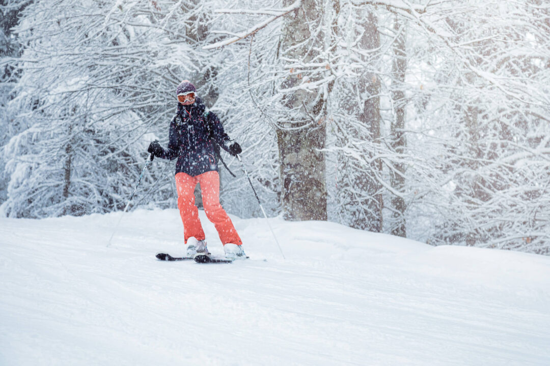 Downhill skier carving fresh powder on a snowy slope through a frosted forest