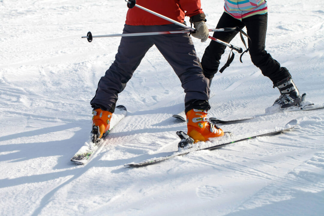 Beginner skiers carving fresh tracks on a snowy downhill slope with ski poles and goggles
