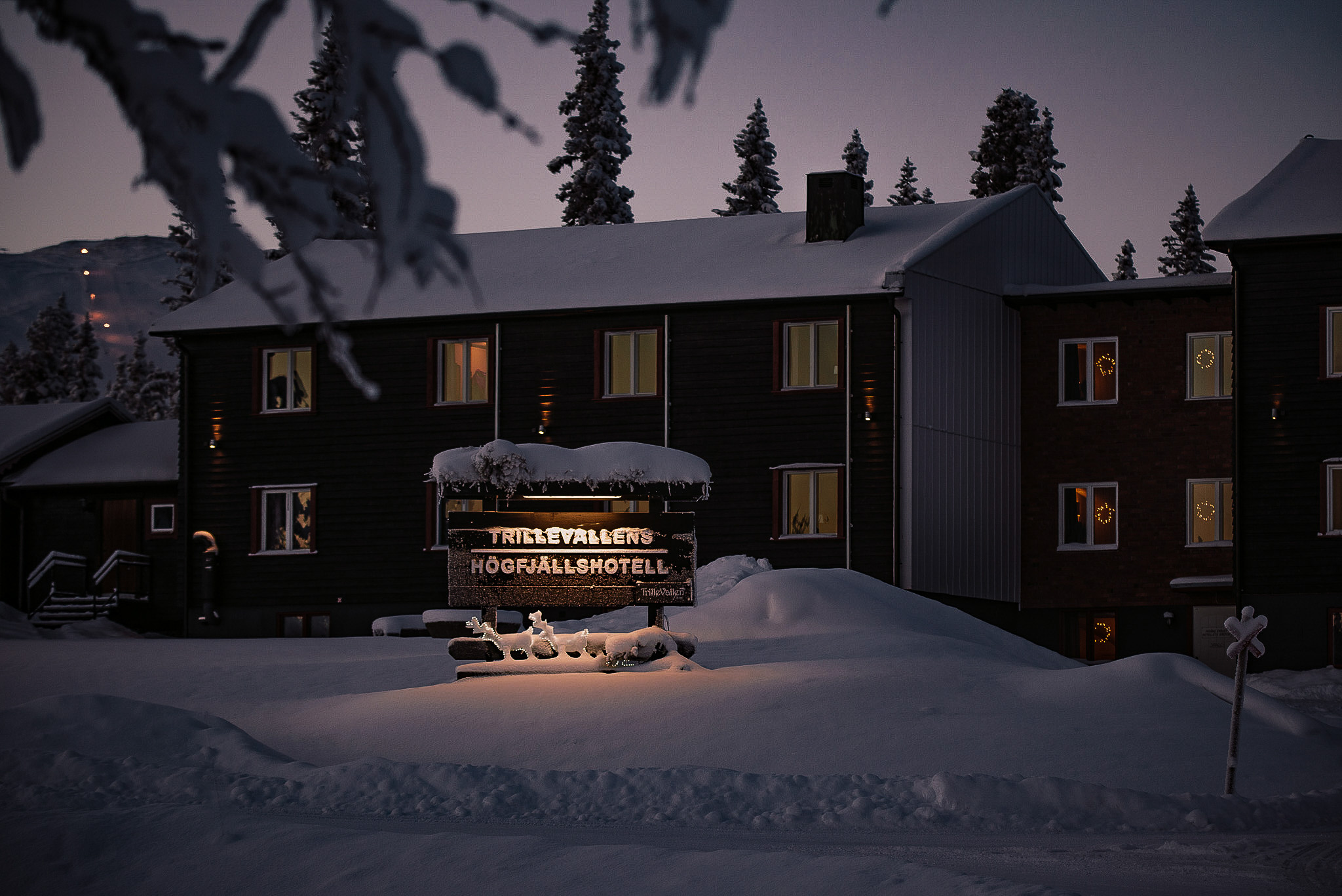 Snowy Swedish ski lodge at dusk with warm-lit windows and a welcome sign outside