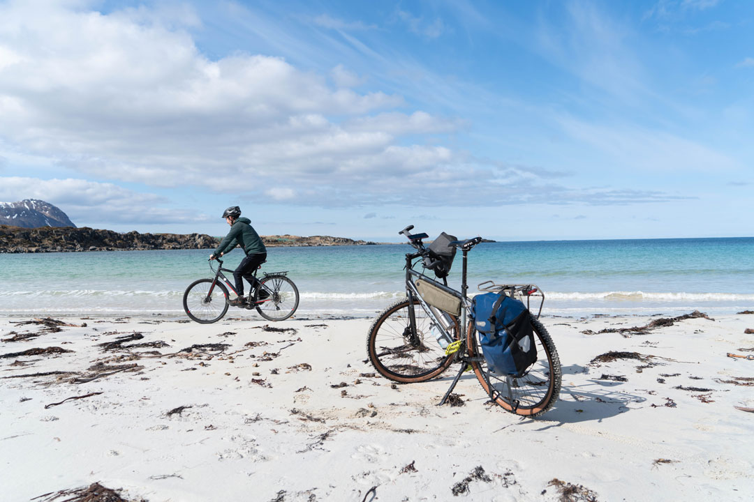 Woman bikepacking along a sandy beach with sea views and pannier-equipped bikes