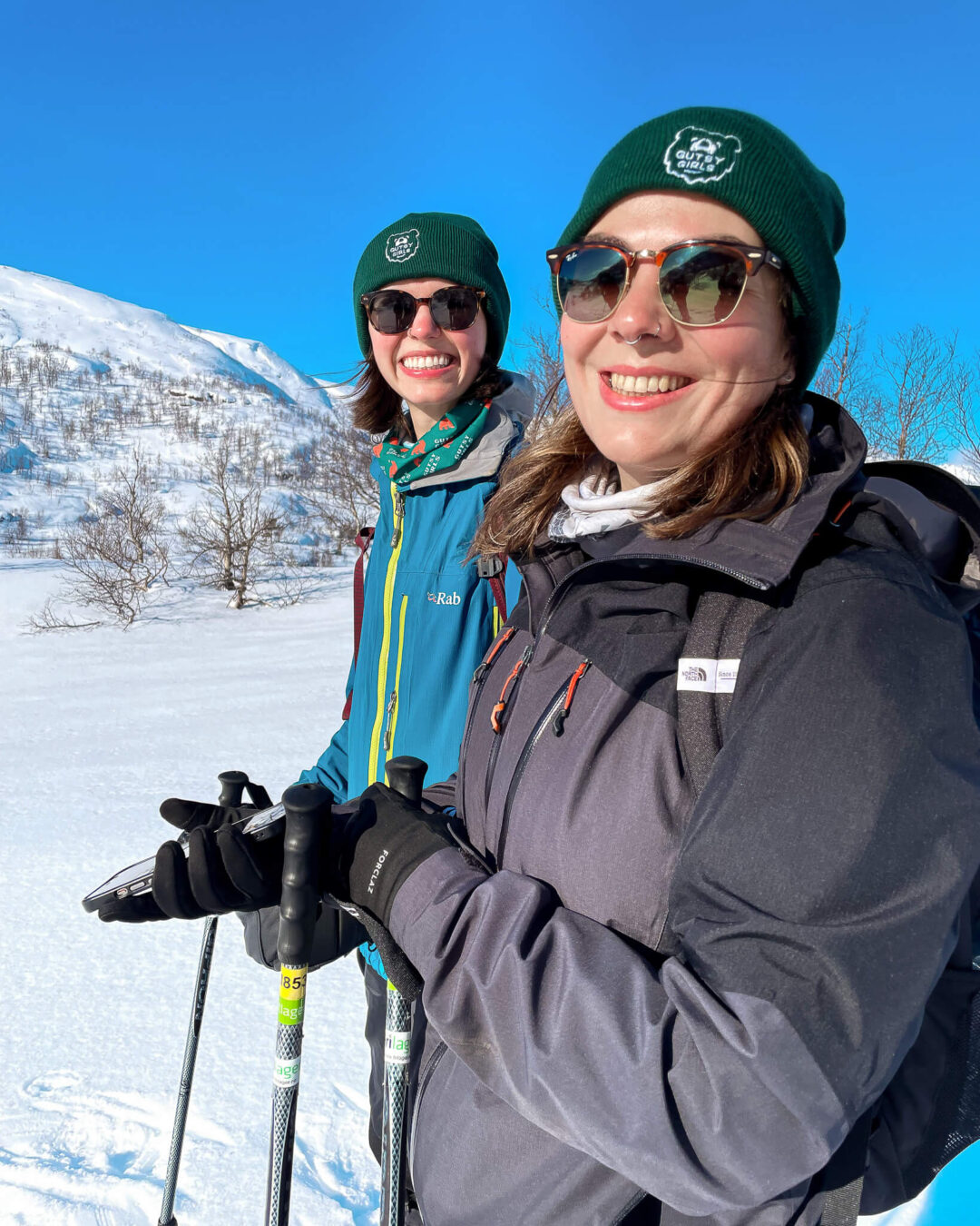 Smiling women snowshoeing on a snowy mountain slope with trekking poles in clear winter sunshine