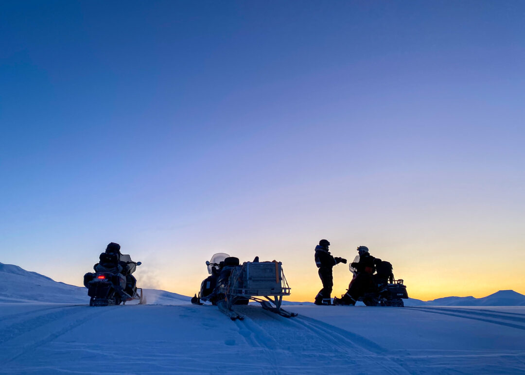 Silhouetted snowmobilers with snowmobiles on Arctic snow at dusk, snowy Svalbard landscape